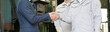 © kapinon - A sales representative and a factory worker shaking hands in a manufacturing plant, symbolizing a relationship of trust; scenes of business contracts and agreements; imagery of B2B without face baneer