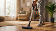 © Laura - Person's lower body using a modern cordless stick vacuum cleaner on a shiny wooden floor in a bright living room.