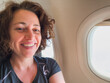 © Юлия Завалишина - Happy passenger young woman is flying in plane. Smiling girl sitting in airplane near window going on trip vacation travel. Traveling female inside plane enjoying flight. Traveling girl