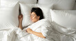 © LAB IMAGE - A peaceful young woman with dark hair sleeping soundly in a comfortable bed surrounded by soft white pillows and a duvet, enjoying deep rest.