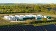 © AmazingAerialAgency - Aerial view of Tiln Photovoltaic Solar Farm and Battery Energy Storage System with white storage containers and solar panels surrounded by lush green trees in Retford, England, United Kingdom.