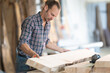 © KONSTANTIN SHISHKIN - Woodworker carefully inspecting raw lumber in carpentry workshop