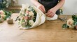 © spyrakot - Florists hands wrapping bouquet in soft neutral paper with twine