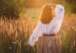 © Soloviova Liudmyla - free-spirited woman in boho outfit walking away through golden meadow at sunset holding straw hat and enjoying serenity of nature during peaceful evening stroll in countryside landscape