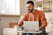 © Pixel-Shot - Handsome young man with cup of tea using laptop in living room