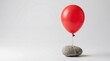 © Emanuel - Red balloon tied to stone symbolizing limitation and freedom contrast