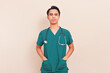 © Muhammad Alimaki - Confident Southeast Asian male doctor in green scrubs with stethoscope and hands in pockets. Professional healthcare worker or medical intern on isolated background.