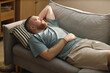 © Seventyfour - High angle view of young adult Caucasian man lying on sofa, resting during house arrest or home confinement. Useful for legal restriction, isolation, detention, stress themes