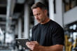 © Milos - A middle-aged man inspects his tablet at a fitness center, embodying the balance between technology and physical health as he navigates his workout regimen.