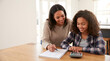 © MULTI SITORUS - smiling mother and daughter doing homework together at wooden table in bright home