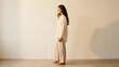 © Enes - Woman in cream linen outfit standing in side profile against beige wall, minimalist fashion portrait