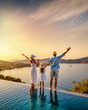 © moofushi - A happy family on summer holidays stands by the swimming pool and enjoys the beautiful sunset behind the ocean