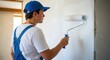 © Momoy Std - Young man in overalls and blue cap paints interior wall with roller