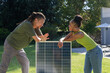 © Wavebreak Media - African American couple leaning on solar panel, man gesturing woman smiling on grassy lawn