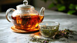 © Aliaksandra - Glass teapot and teacup with loose leaf herbal tea on marble surface, creating a warm and elegant tea ritual scene
