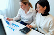 © Mediaphotos - Young businesswomen reviewing financial charts and calculating budget data at office desk. Useful for accounting, teamwork, financial planning, audit, or corporate reporting