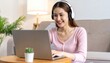 © Umianifaturosidah - Smiling Asian Woman Working on Laptop with Headphones at Home.