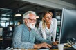 © sogap - older office worker and younger colleague reviewing data on computer