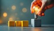 © Viktor - Hand places glowing lightbulb on cube near yellow blocks. Symbolizes new idea innovation startup growth business strategy, concept development progress.