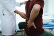 © Kieng - Doctor explaining spine anatomy with a model to a male patient experiencing lower back pain in a clinic, discussing diagnosis and treatment options.