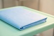 © Tima - Sterile blue paper drape on medical table. Folded surgical sheet for clinical procedure. Equipment for operation in hospital room. Healthcare sanitation and hygiene preparation material.