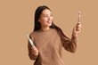 © Pixel-Shot - Young Asian woman with toothbrushes on beige background