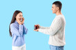 © Pixel-Shot - Boyfriend giving glass of warm mulled wine to his happy girlfriend on blue background