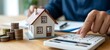 © Amena - person calculating home expenses with model house and coins on desk