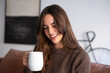 © luciano - Smiling Young Woman Drinking Coffee From White Mug At Home In Cozy Sweater