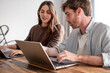 © luciano - Young Colleagues Collaborating on Laptops at a Wooden Table in a Casual Home Office Workspace