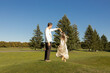 © Anna - Beautiful newlyweds dancing joyfully barefoot on the green grass on a sunny day. A cheerful couple in love, a happy moment, a bride and groom. Ukrainian outfits, a flower wreath