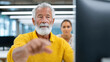 © Chaiwit - Elderly man in yellow sweater learning digital literacy with woman support in modern office environment focused on computer screen