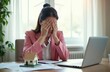 © Pete - Woman in pink jacket hides face in hands at desk with laptop and house model. Feeling overwhelmed by finance, loan, or mortgage issues, real estate problems, workplace frustration and burnout.