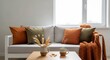 © phy - A cozy living room with a white couch adorned with orange and green pillows, a wooden coffee table with a vase of dried flowers, and a blanket draped over a chair.