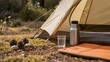 © Наталия Пилипенко - Camping tent with a stainless steel thermos and a glass of water on the ground. Concept of outdoor adventure, hiking equipment, camping life, and hydration during trekking in nature
