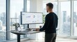 © Thea - Professional man working at standing desk with large monitor displaying business analytics and data charts in modern office with city view window background, remote work concept