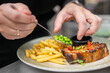 © pavel siamionov - A chef garnishes a plate of honey-glazed pork belly and crispy French fries with fresh green peas, adding a vibrant touch to the gourmet dish in a professional kitchen