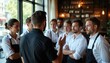 © Vadym - Restaurant manager talks to staff before shift. Team listens attentively to leader giving guidance. Employees in uniform work together in hospitality setting. Coordination, communication for service
