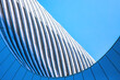 © Newleks - Modern building facade featuring dynamic architectural curves and flowing lines under a bright blue sky, creating an abstract geometric pattern with sleek steel and glass panels