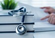 © twilight mist - Medical stethoscope rests on a stack of textbooks while a student studies in the background.