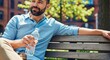 © Angavlan - Man with water bottle relaxing on city bench enjoying sunny day in park. Casual outfit includes light blue shirt and beige pants. Ideal for wellness and lifestyle content featuring men.