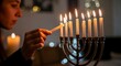 © Sagheeran - Woman lighting hanukkah menorah with candles in a dark room
