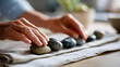 © Kateryna - Close up of hands gently arranging a row of smooth pebbles in ascending size on a clean bright linen cloth mindful arranging zen practice meditative placing ordered pebbles