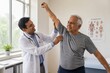 © Natallia Simanchyk - An Indian doctor examines a senior man's shoulder during a physical therapy session. The scene highlights professional healthcare and rehabilitation. Ideal for medical or wellness content.