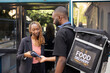 © DC Studio - Black delivery man with pos terminal as the female customer pays with phone, using nfc system transaction for her restaurant takeaway. Transaction completes the meal delivery efficiently.