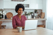 © Dragana Gordic - Smiling Woman Working on Laptop in Bright Kitchen Home Office During Remote Work Session