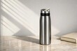 © melano - Stainless steel reusable water bottle on a marble surface with books and artistic window light shadows on a neutral wall.