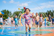 © Meow Creations - Happy asian toddler girl running through water sprays at sunny outdoor splash pad