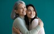 © Xo - Young woman hugging her smiling mother from behind on turquoise background.