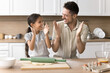 © fizkes - Dad and daughter having fun, clap hands smeared with white flour looking at each other with love while cooking together, preparing homemade dough for holiday cake or pie in modern kitchen. Culinary